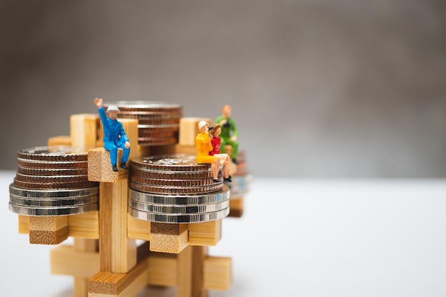 Miniature people, business team sitting on stack coins 