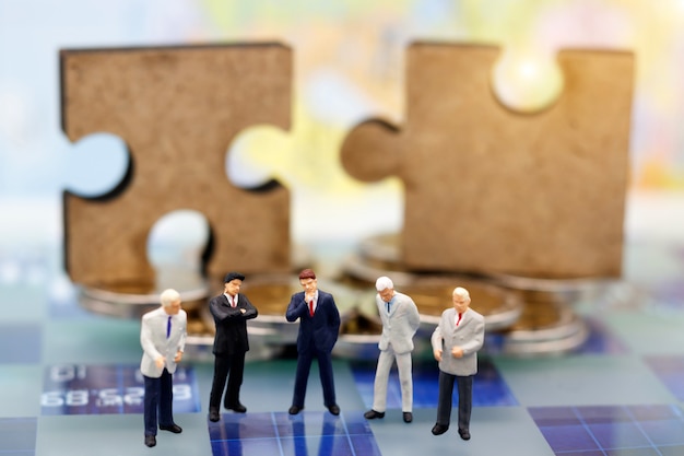 Miniature people, businessman are thinking with jigsaw puzzle on coins stack.