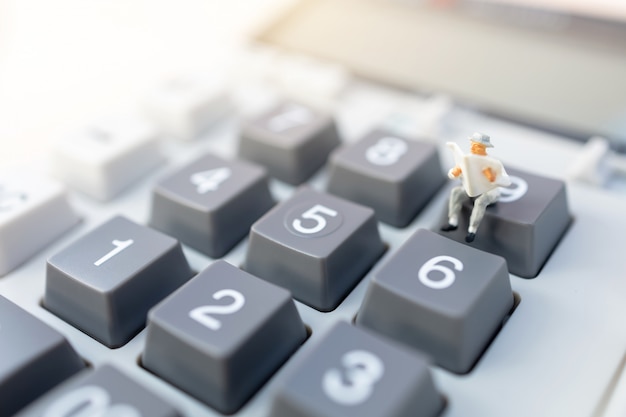 Miniature people: Businessman reading on calculator. Financial and business concept