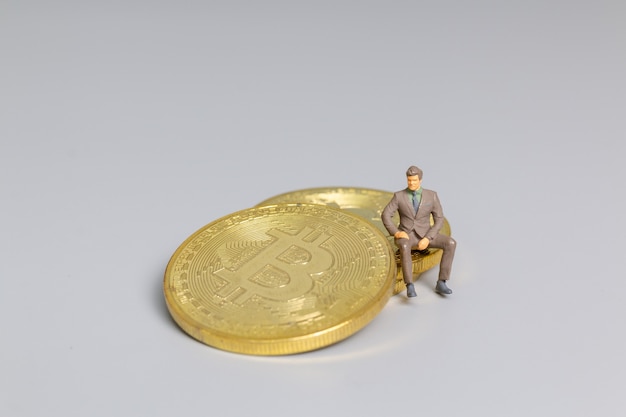 Миниатюрные люди бизнесмен, сидящий на монетах Bitcoin