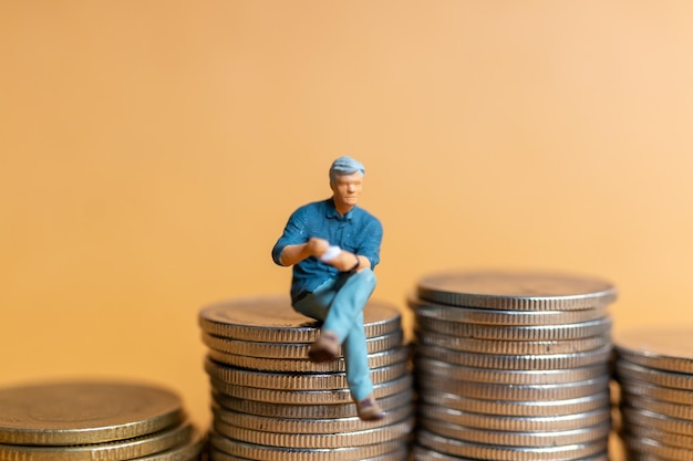 Miniature people Businessman sitting on coins stack