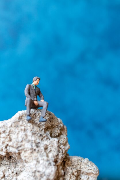 Miniature people Businessman sitting on the rock with blue background