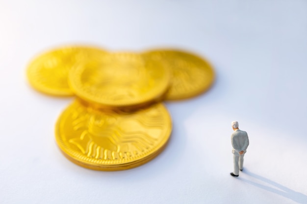 Persone in miniatura: imprenditore stare e pensare a monete d'oro, la crescita nel concetto di business.