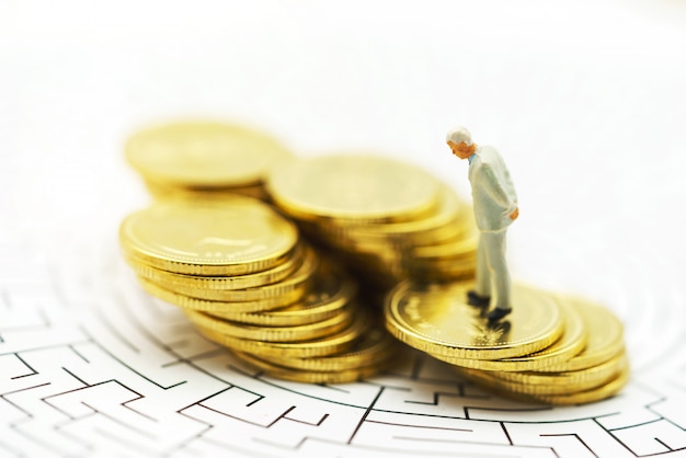 Miniature people: Businessman standing on center of maze with coins stack. 