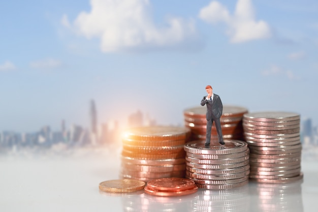 Miniature people: businessman standing on coin stacking podium