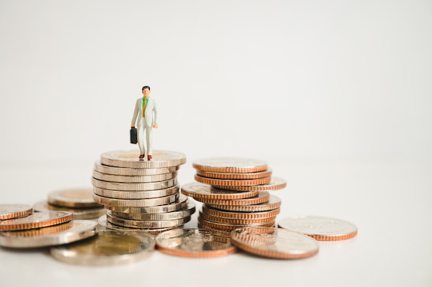 Miniature people, businessman standing on pile coins 