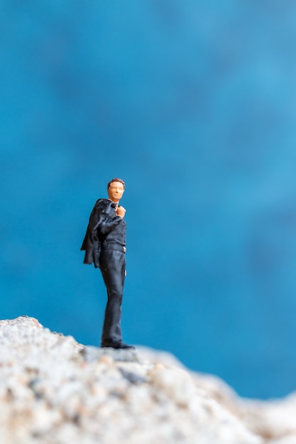 Miniature people Businessman standing on the rock with blue background