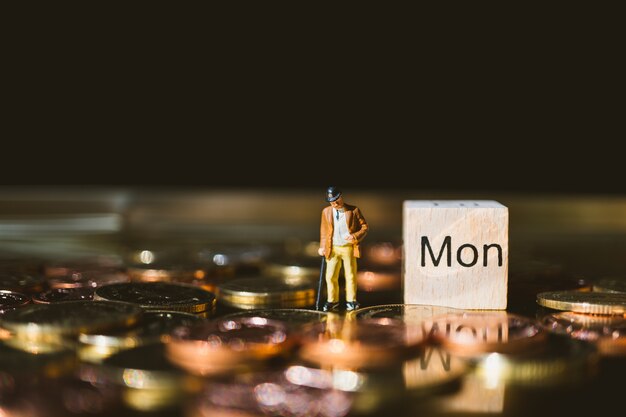 Миниатюрные люди, бизнесмен, стоя с монетами золотого стека и деревянный блок в понедельник, используя в качестве busi