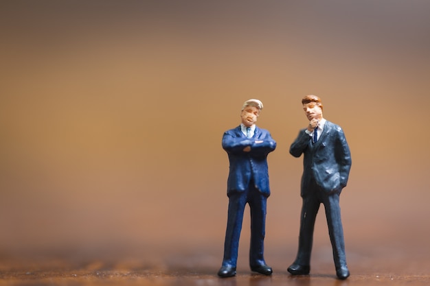 Miniature people Businessman standing on wooden background 