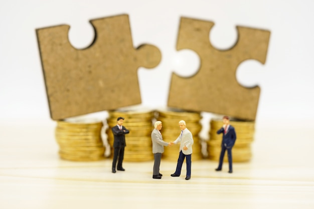 Miniature people: Businessmen handshake with jigsaw on coins stack. Finance .