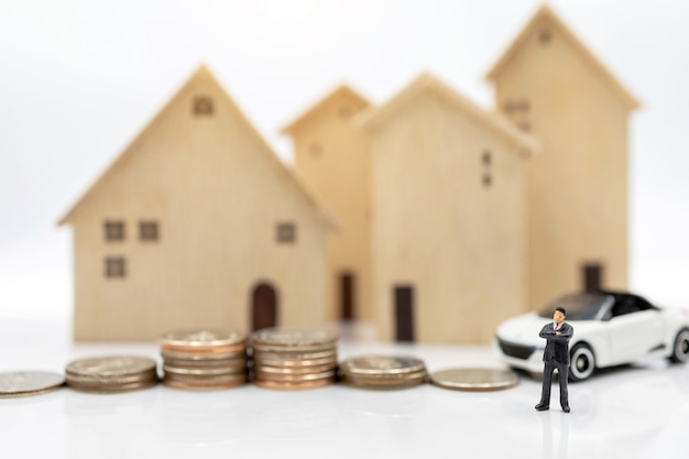 Photo miniature people:  businessmen shaking hands on coins stack with house and car.  concept of investment in housing and vehicles.