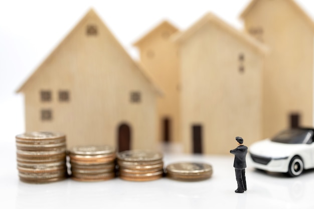 Miniature people:  Businessmen shaking hands on coins stack with house and car.  Concept of investment in housing and vehicles.