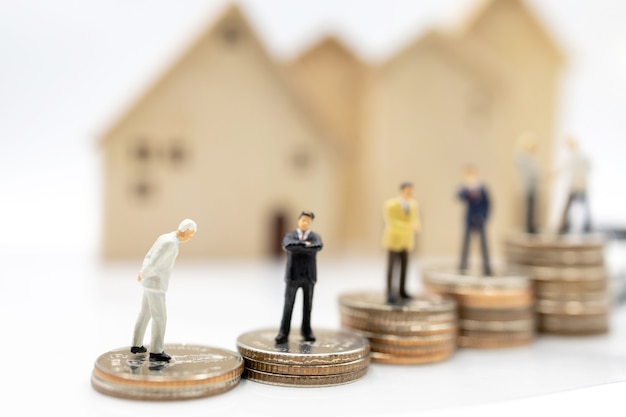 Persone in miniatura: uomini d'affari che si stringono la mano sulla pila di monete con casa e auto. concetto di investimento in abitazioni e veicoli.