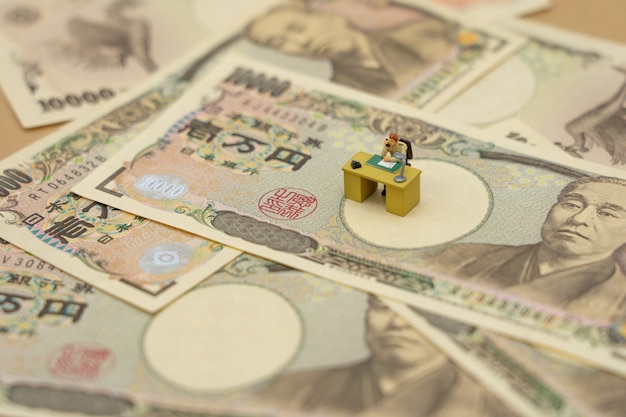 Uomini d'affari in miniatura che siedono con banconote giapponesi del valore di 10.000 yen