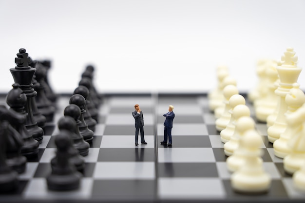 Miniature people businessmen standing on a chessboard with a chess piece 