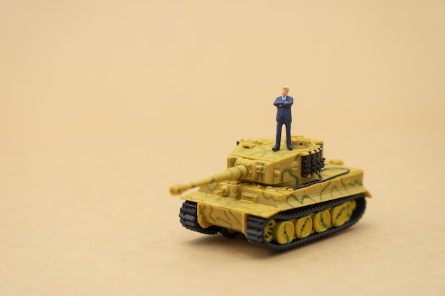 Miniature people businessmen standing with a tank model on the back negotiating