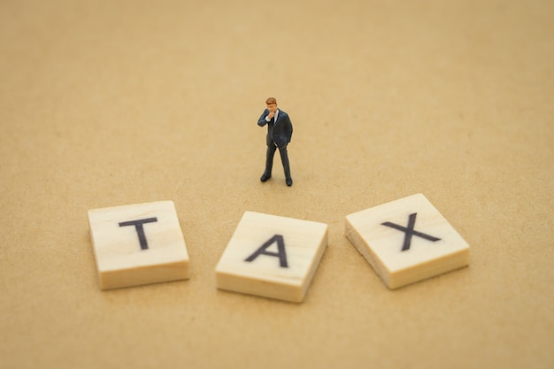 Miniature people businessmen standing with wood word TAX 