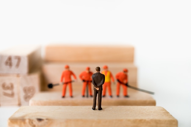 Miniature people, chief and engineer team standing on wooden block