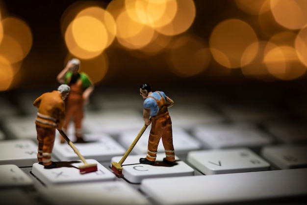 Photo miniature people cleaning white keyboard computer.