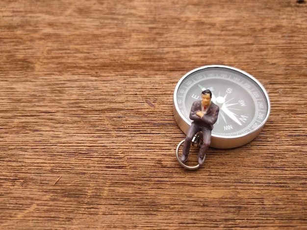 Miniature people and compass with copy space on a wooden background