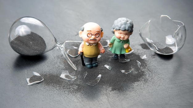 Miniature people couple of elderly people near a broken hourglass life time crisis the concept of the end of life for a person