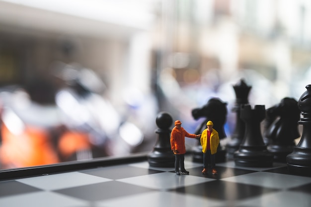 Miniature people, couple engineers standing on chess board