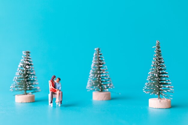 Miniature people, Couple in love sitting next to a Christmas tree , Christmas and Happy New Year concept.