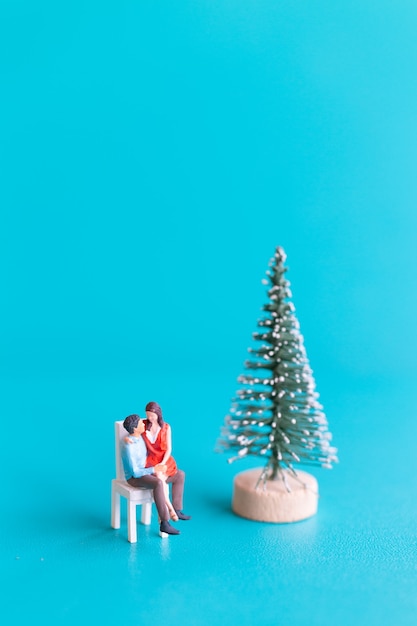 Miniature people, Couple in love sitting next to a Christmas tree , Christmas and Happy New Year concept.