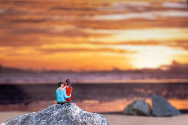 Miniature people Couple sitting on a sea beach with sunset background