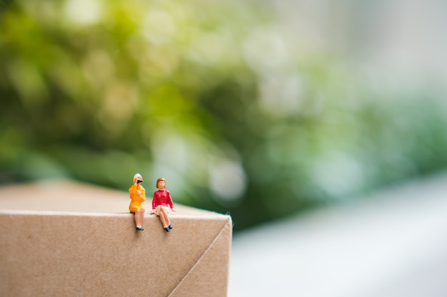 Miniature people, couple woman sitting on paper box using as business and social concept