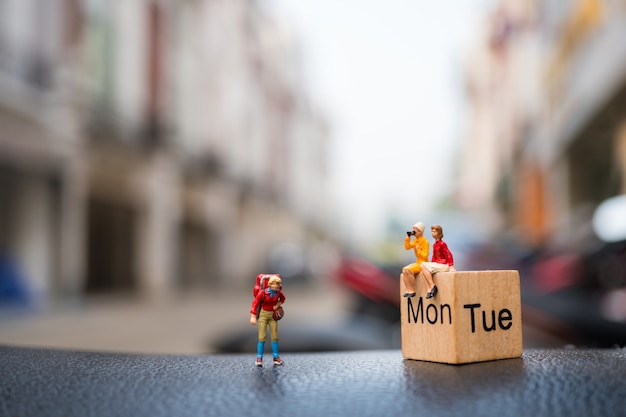 Miniature people, couple woman sitting on wooden block calendar with traveler woman using as busines
