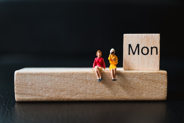 Miniature people, couple woman sitting on wooden block using as business concept