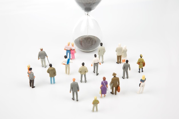 Miniature people different people are walking next to the hourglass on a white background lifespan of humanity