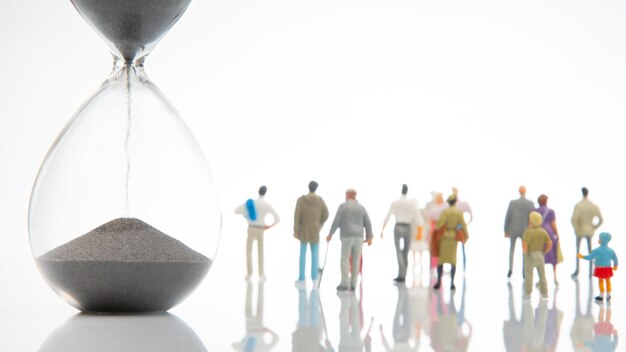 Miniature people different people are walking next to the hourglass on a white background lifespan of humanity