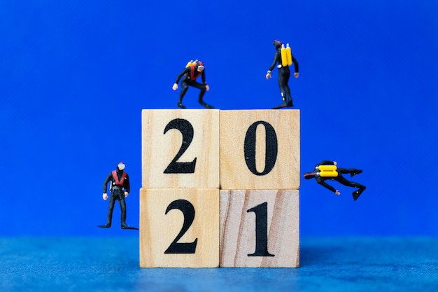 Miniature people divers diving around wooden block 2021, Happy new Year concept