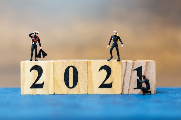 Miniature people divers diving around wooden block 2021, Happy new Year concept