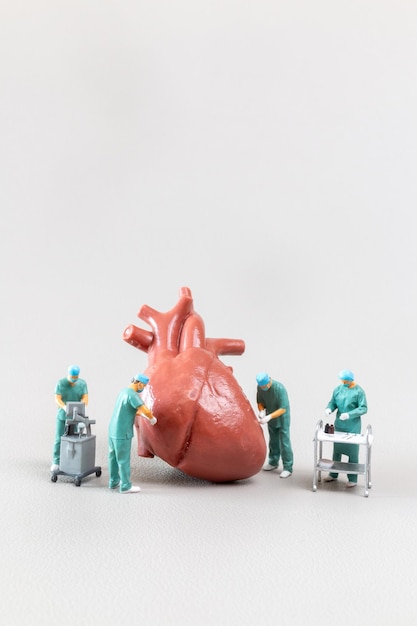 Foto persone in miniatura medico che controlla e analizza modello di cuore su sfondo blu concetto di scienza e medicina