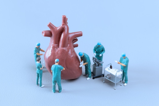 青色の背景にミニチュアの人々の医師のチェックと分析の心臓モデル 科学と医学の概念