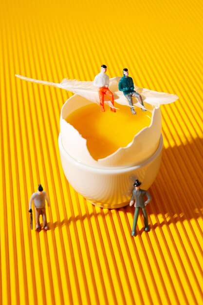 Miniature people and egg on textured yellow background