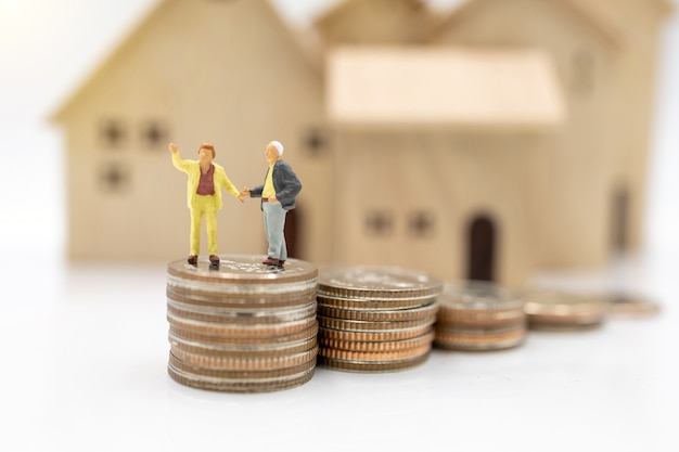 Photo miniature people: elderly person standing on coins stack with home, retirement planning concept.