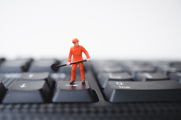 Miniature people, engineer standing on computer keyboard 