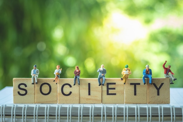 Miniature people, group of business people sitting on wooden blocks with SOCIETY word.