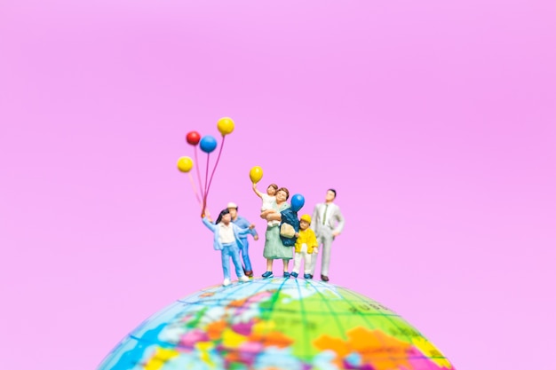 Miniature people : Happy family holding balloon on The globe with pink background 