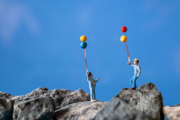 Miniatura persone, felice famiglia azienda palloncino sulla roccia con cielo blu