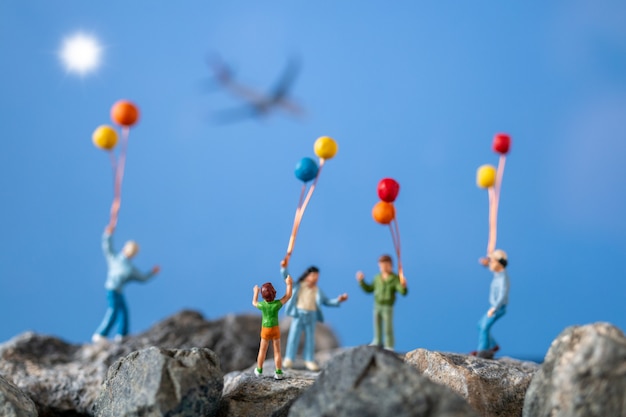 Photo miniature people , happy family holding balloon on the rock with blue sky