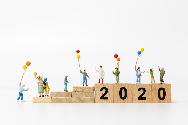 Miniature people: Happy family holding balloon on wooden block number 2020 