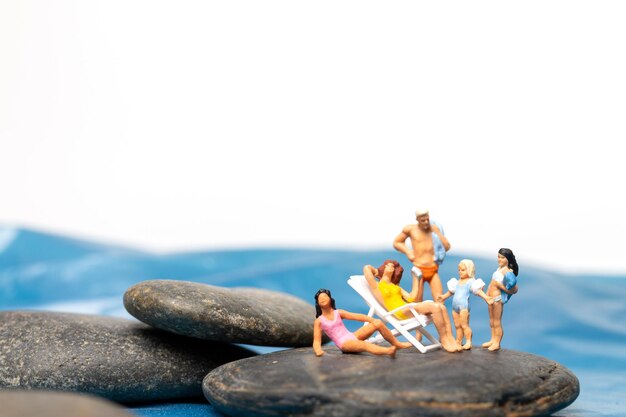 Photo miniature people happy family sitting on the large rocks near the coast with blue sea