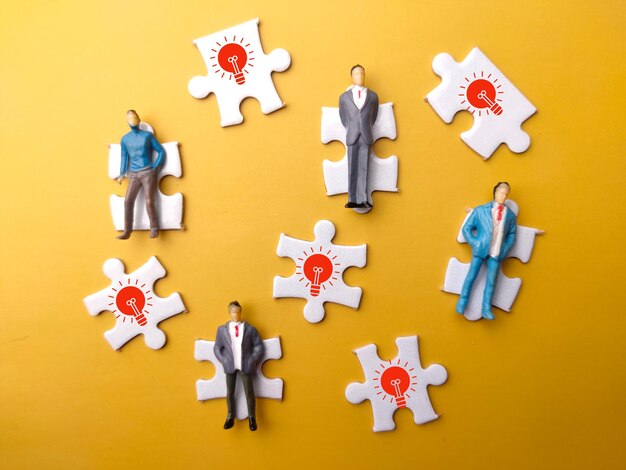 Miniature people and idea icon with white puzzle on a yellow background