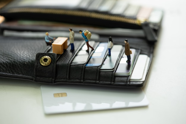 Miniature people in line at the bank counter on the purse filled with credit card.