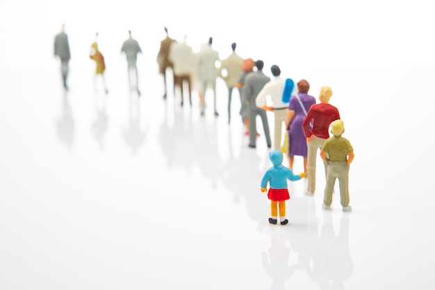 Miniature people little girl stands against the background of other people on a white background Loneliness and family acceptance in human society Child care